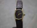 Front 3/4 view of the Raymond Weil hexagonal watch on a dark stand, showing the burgundy dial, gold case, and brown lizard-style leather strap.
