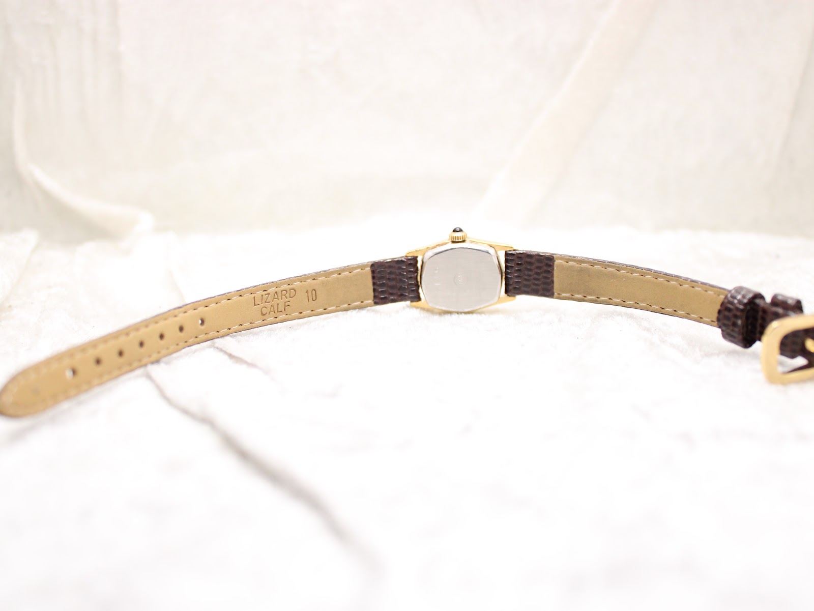 View of the watch laid flat, showing the inner lining of the brown leather strap with "LIZARD CALF 10" text and the stainless steel case back.