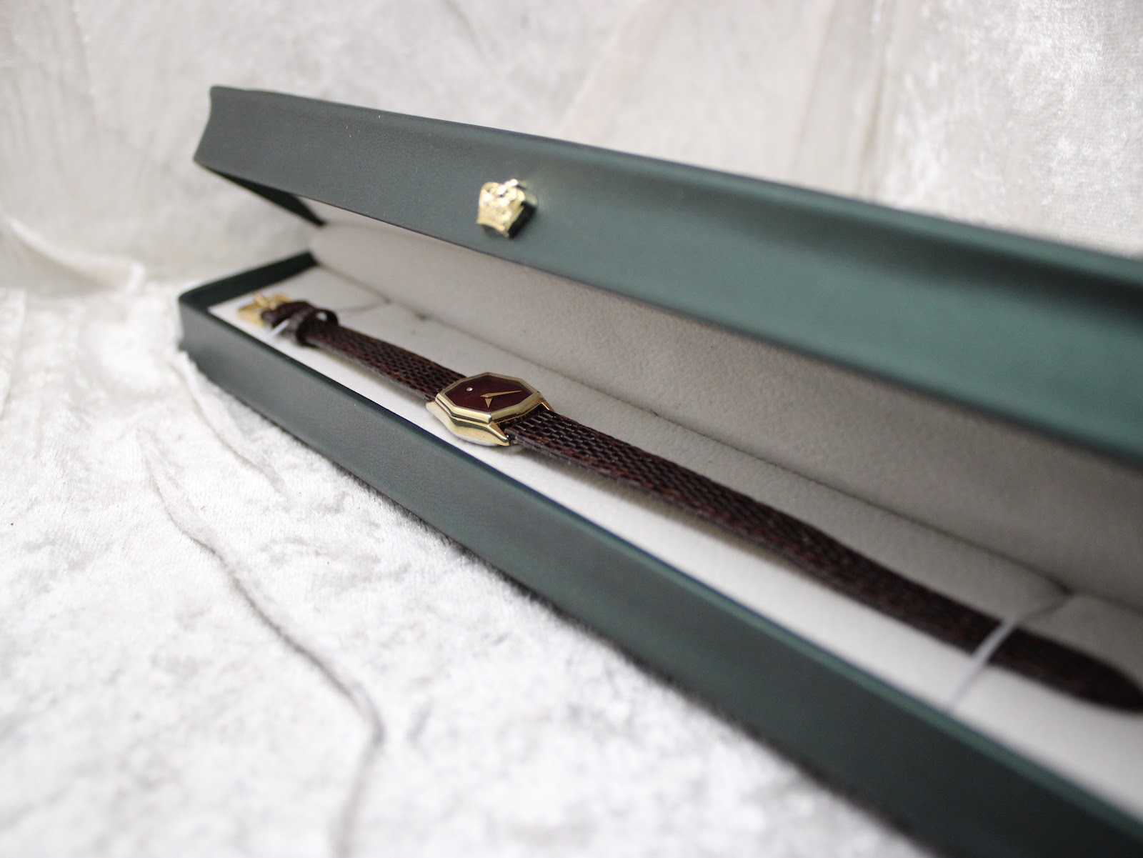 The Raymond Weil watch resting in a dark green presentation box, open to display the watch and strap on a white liner.