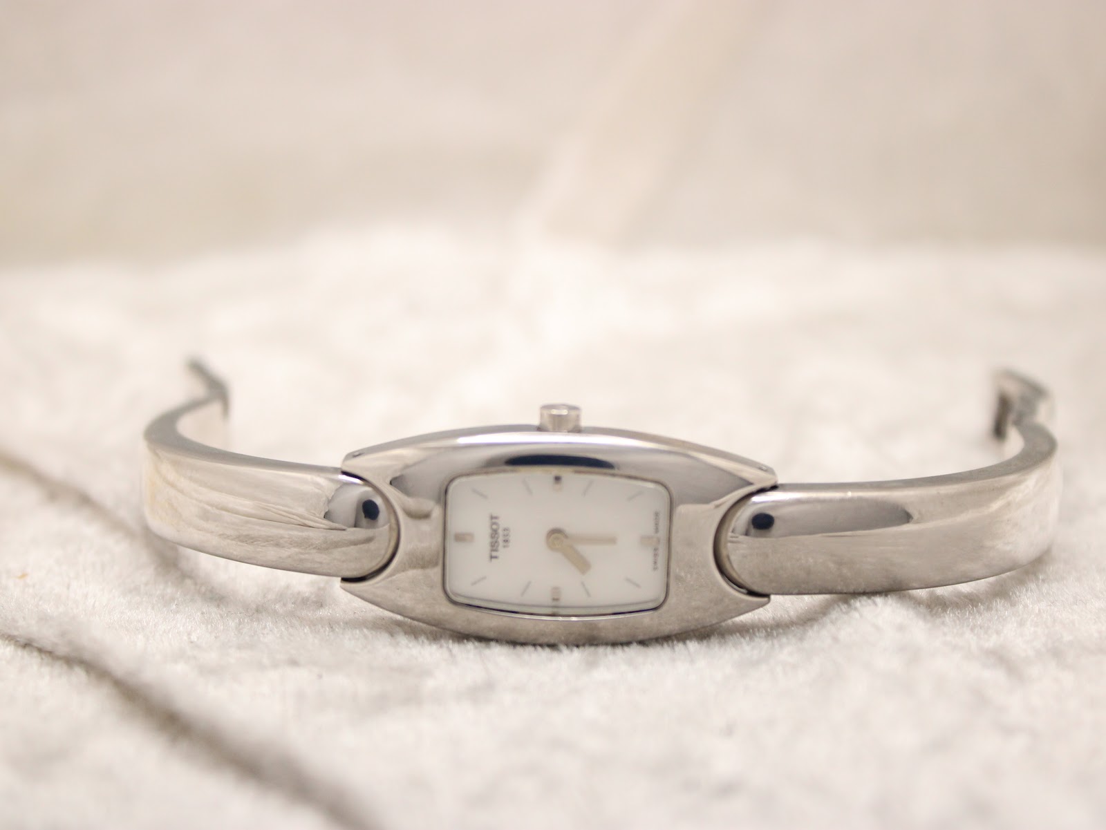 Full front view of the Tissot C845 watch laid flat on a white textured surface, showcasing the integrated stainless steel bangle.