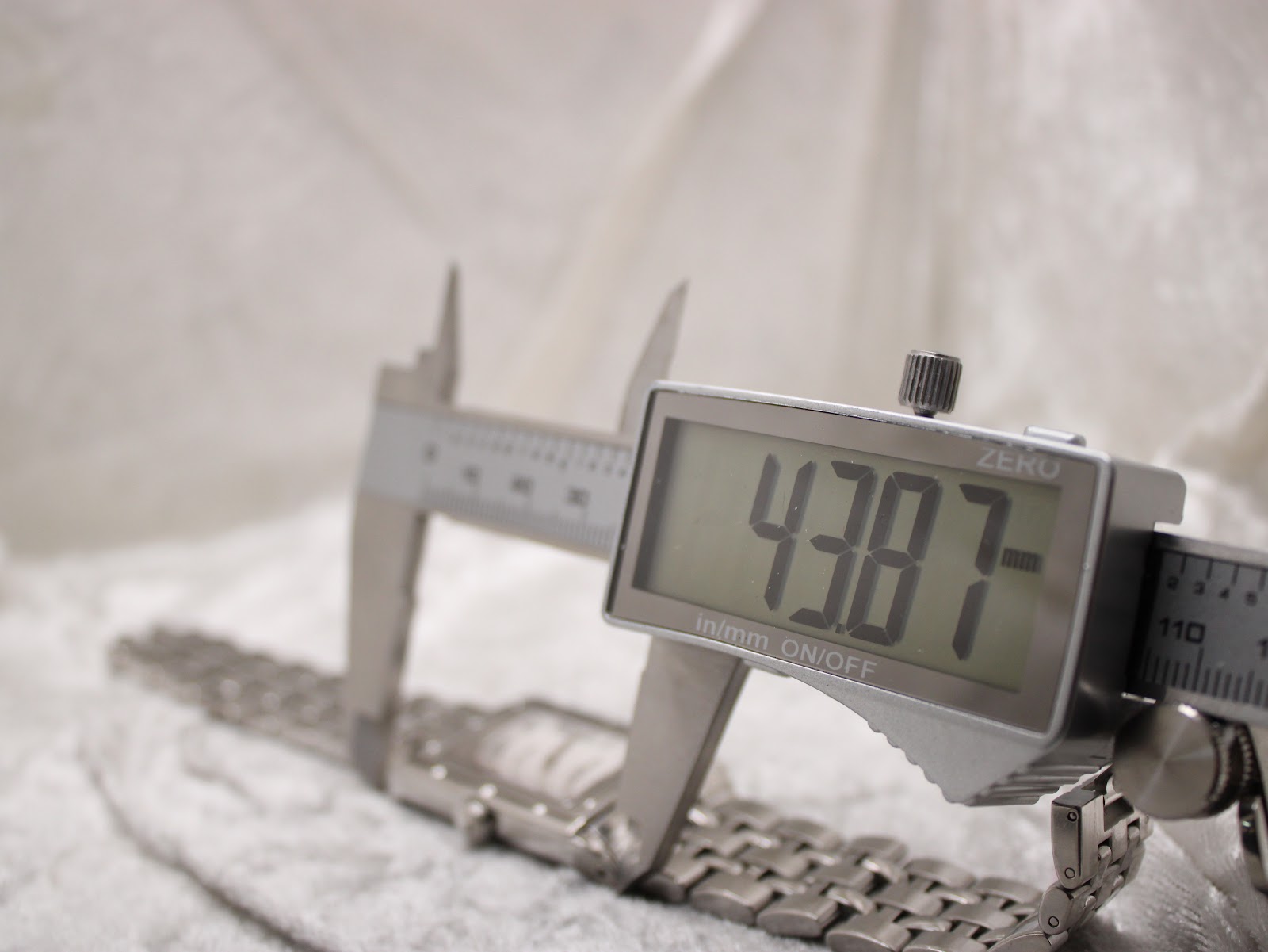Digital caliper measuring the watch lug-to-lug length at 43.87mm, with the watch resting on a support.