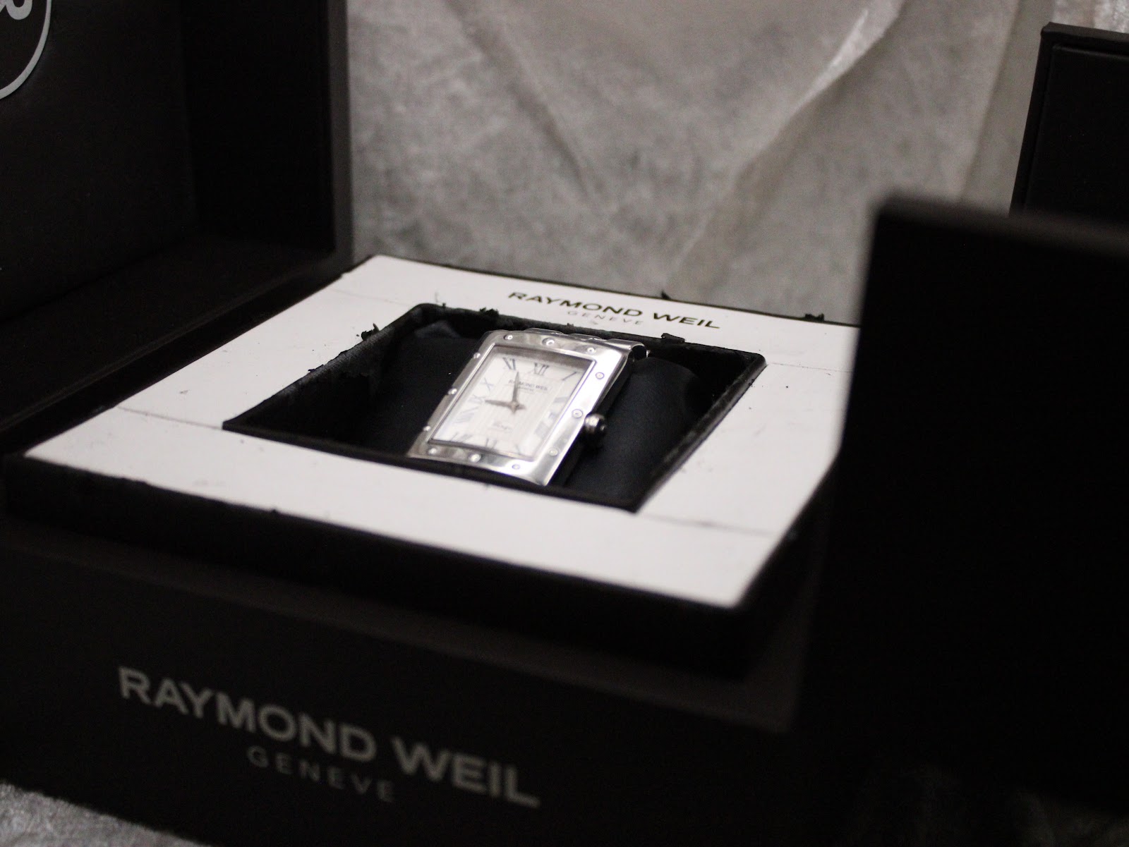 Angled top-down view of the Raymond Weil Tango watch nestled within its black box interior.