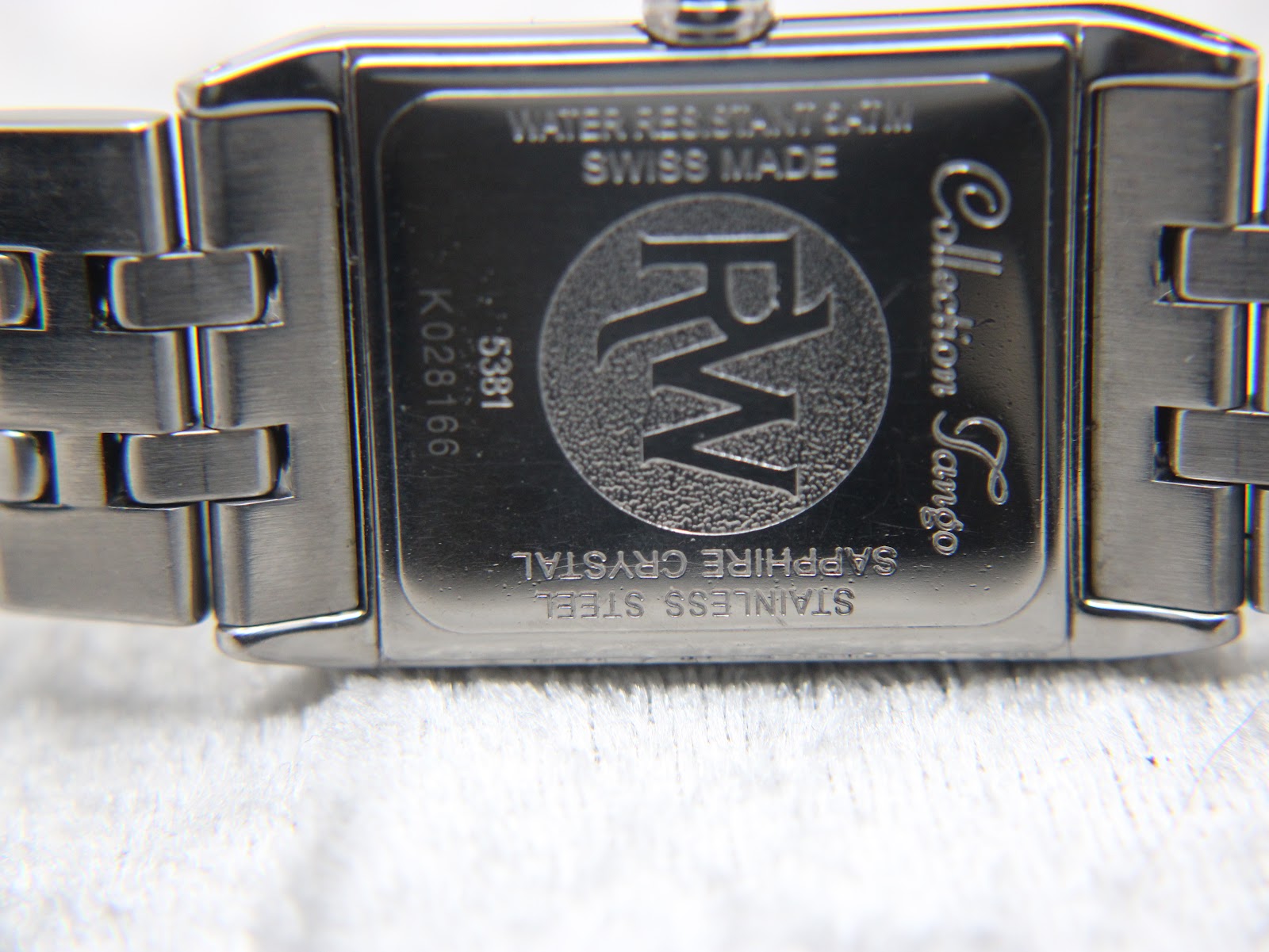 Close-up of the watch case back engraved with 'WATER RESISTANT 5ATM', 'SWISS MADE', 'SAPPHIRE CRYSTAL', 'STAINLESS STEEL', 'Collection Tango', model 5381, and serial K028166.