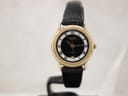 Front view of Raymond Weil ladies' quartz watch with gold-tone case, black dial, white Roman numerals, and black leather strap on a watch stand.
