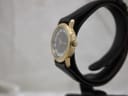 Side profile of the gold-tone Raymond Weil watch, showing the crown and polished case on a black watch stand.