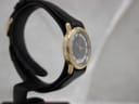 Another side profile of the gold-tone Raymond Weil watch, showing the lugs and case side on a black watch stand.