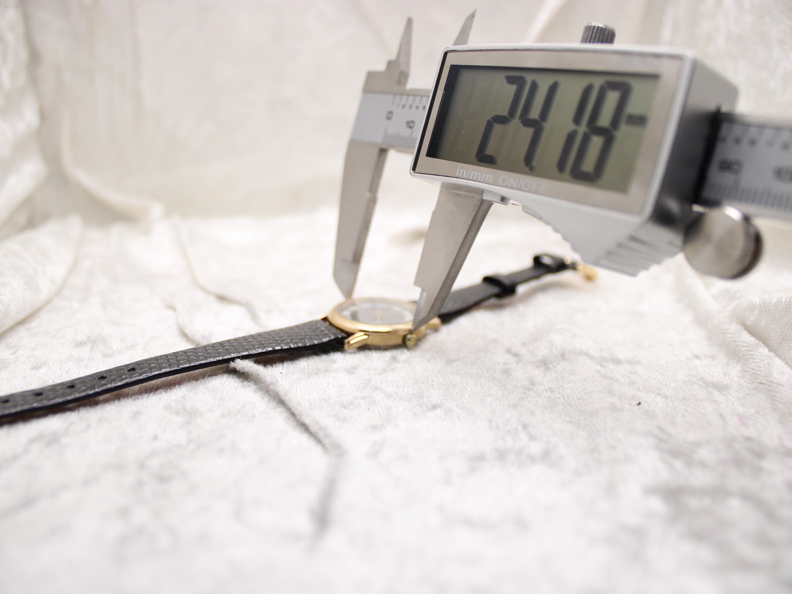 Digital caliper measuring the case diameter of the Raymond Weil watch, displaying a reading of 24.18mm.