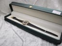 The Raymond Weil watch with black leather strap neatly presented inside a dark green presentation box with cream interior.