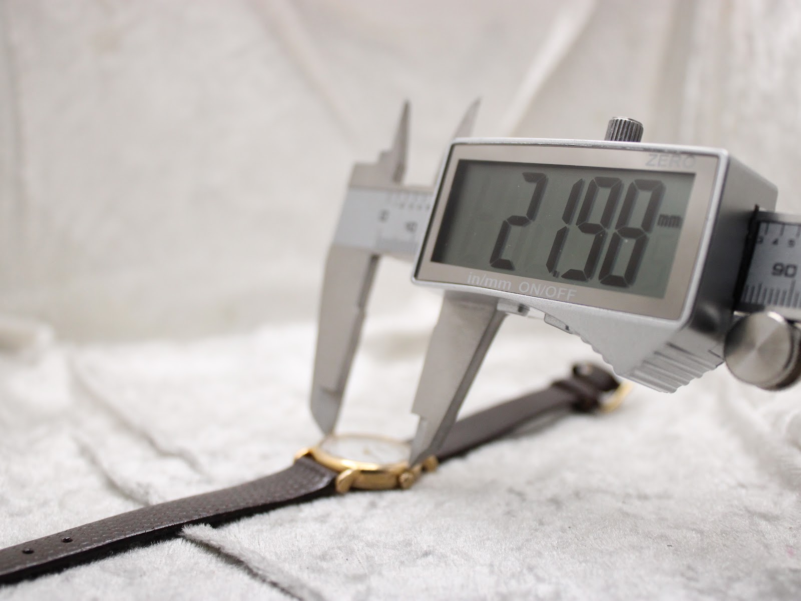 Digital caliper measuring the case diameter of the Raymond Weil watch, displaying a precise measurement of 21.98mm.
