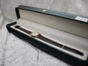The Raymond Weil watch, with its brown strap, presented inside an open dark green box with a cream-coloured interior.