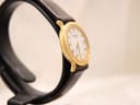 Angled side view of the Raymond Weil watch on a stand, showing the gold case and textured brown leather strap.
