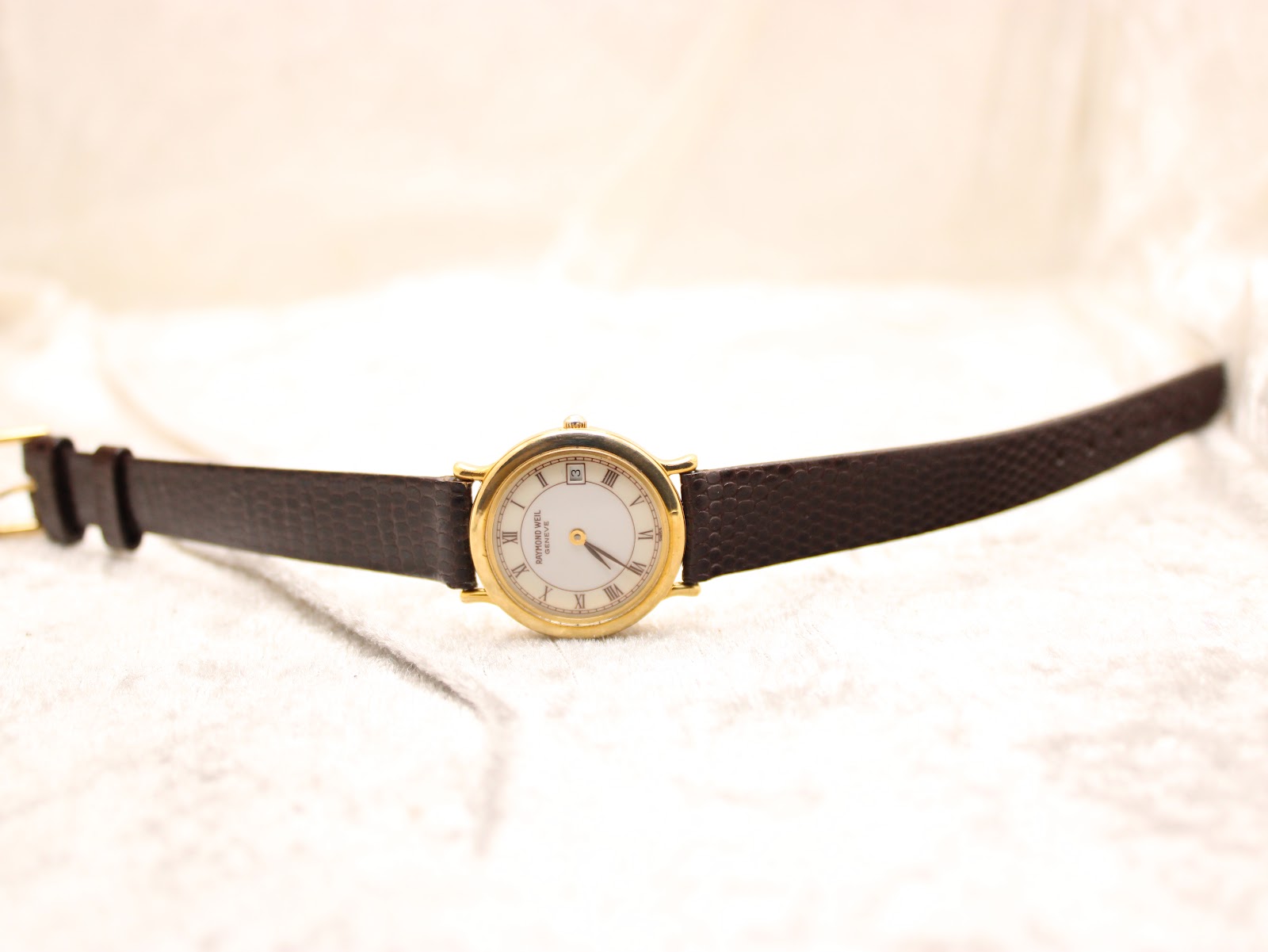 Full view of the Raymond Weil watch with its brown leather strap extended on a light, textured surface.