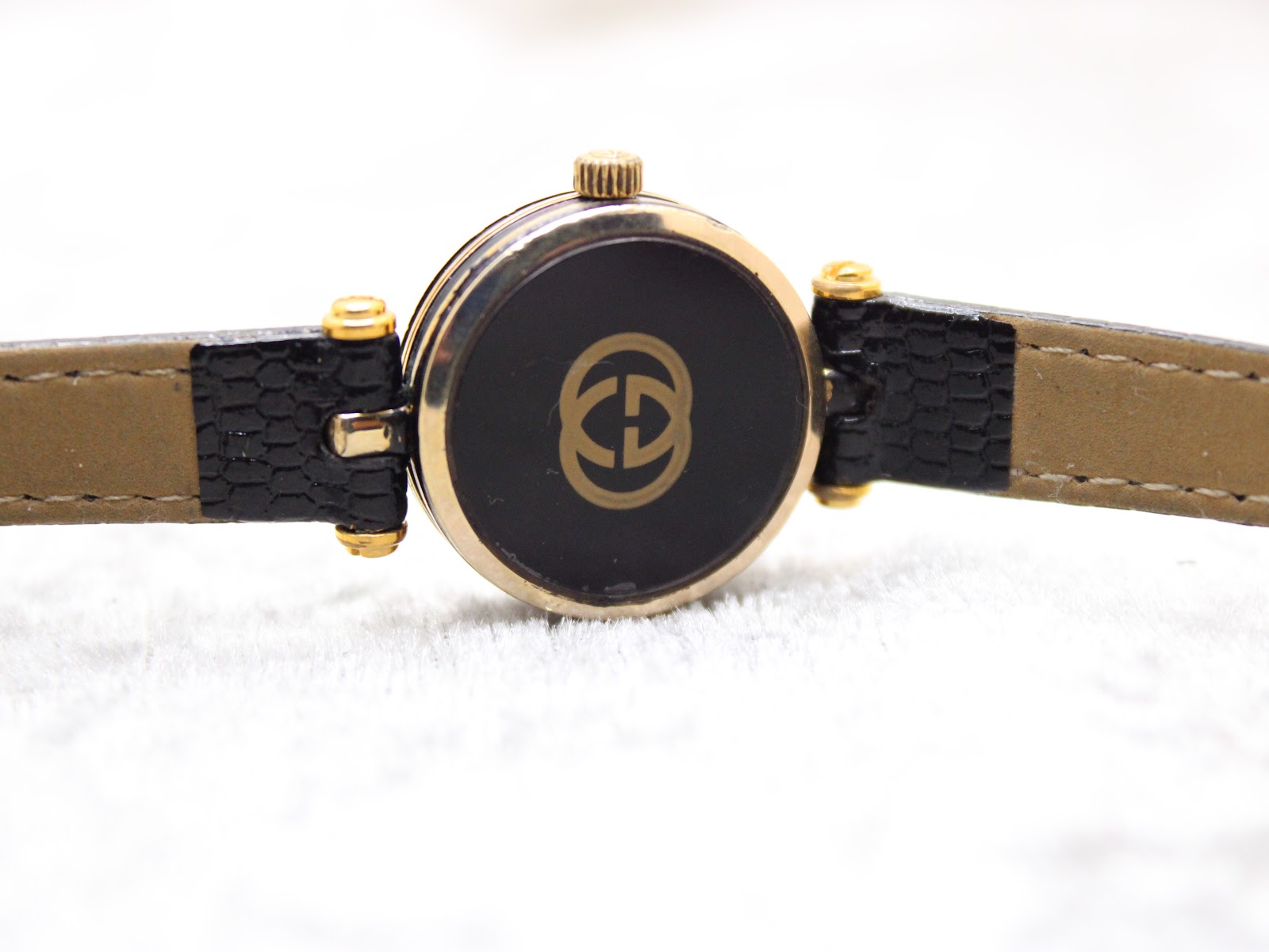 Top-down view of the Gucci 2000L case back, featuring the gold interlocking G logo on a black background.