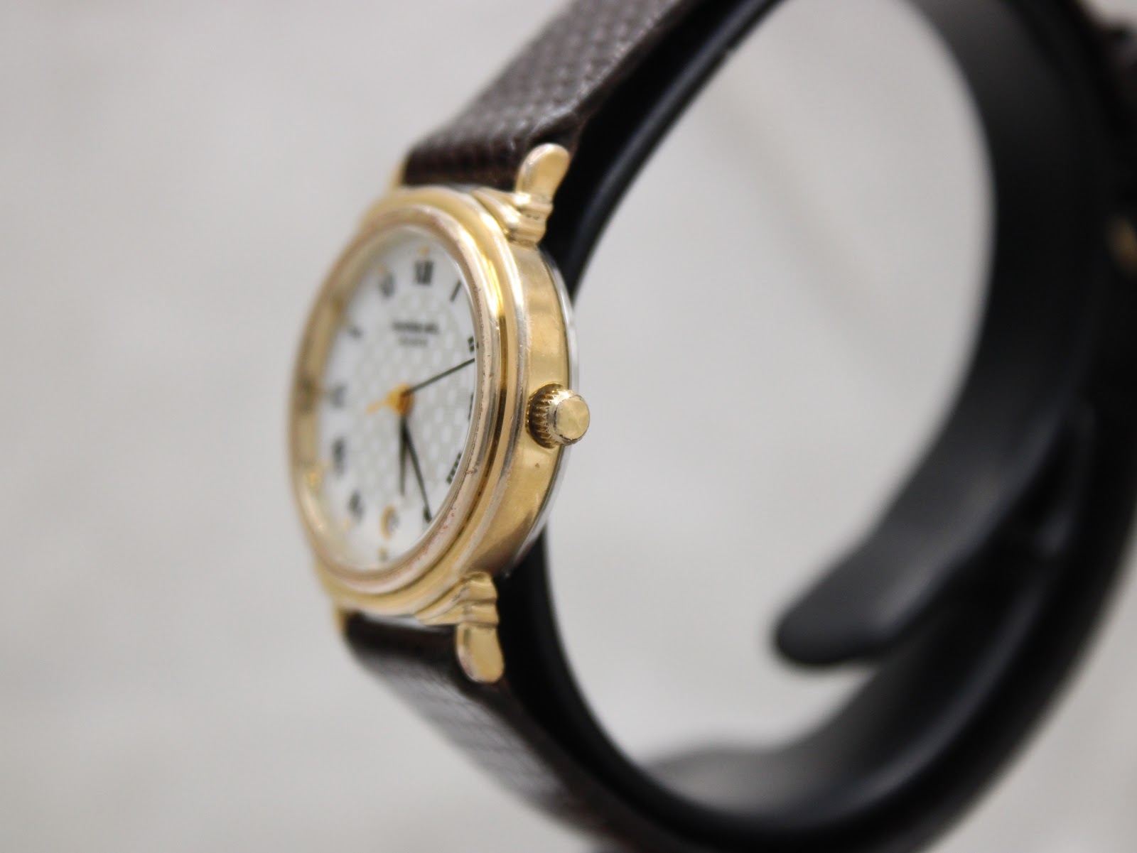 Right side view of the Raymond Weil 5331 watch, showing the gold-plated case and crown on a stand.