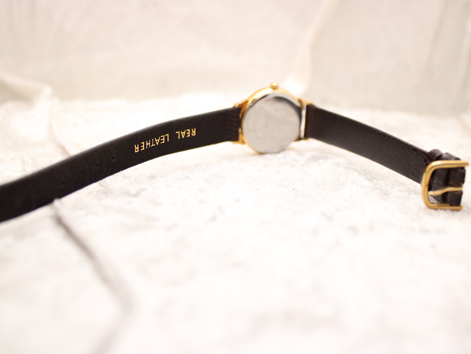 Back view of the Raymond Weil 5331 watch and brown leather strap, showing the gold-tone buckle and 'real leather' embossing.