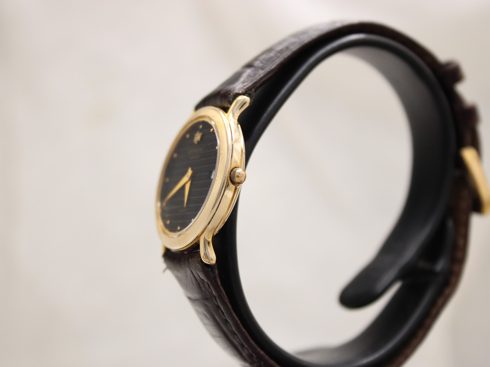 Side view of the Raymond Weil watch showing the slim gold electroplated case and gold-tone crown, with the black leather strap.
