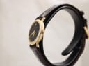 Side view of the Raymond Weil watch showing the slim gold electroplated case and gold-tone crown, with the black leather strap.