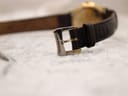 Close-up of the Raymond Weil signed buckle on the black leather strap.
