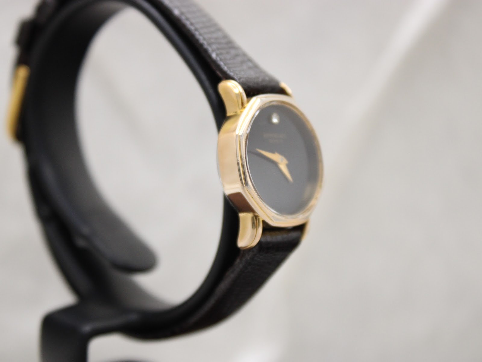 Angled side view of the Raymond Weil Geneve watch on a display stand, highlighting the slim gold-tone case and black strap.