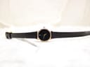 Full length top-down view of the Raymond Weil Geneve watch with its black leather strap laid flat on a white textured surface.