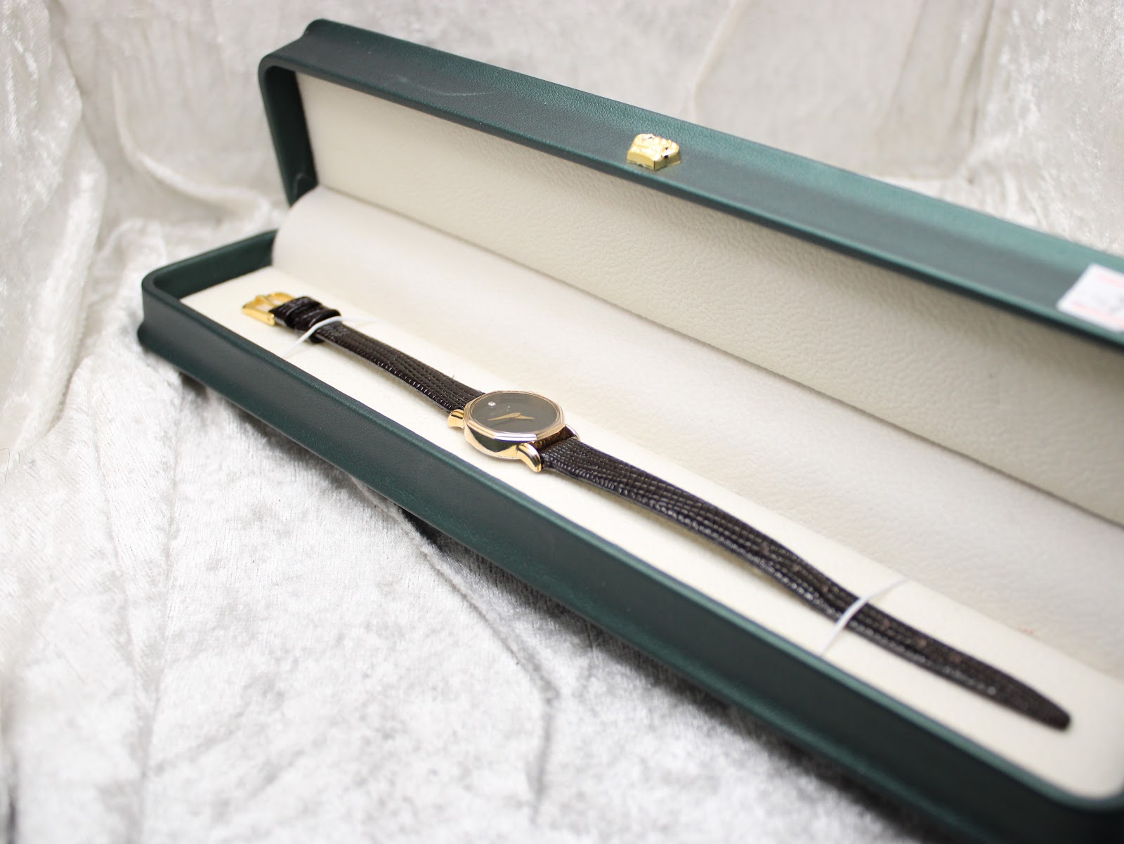 The Raymond Weil Geneve watch resting inside an open dark green presentation box with a cream-coloured interior.