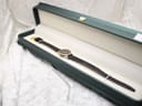 The Raymond Weil Geneve watch resting inside an open dark green presentation box with a cream-coloured interior.