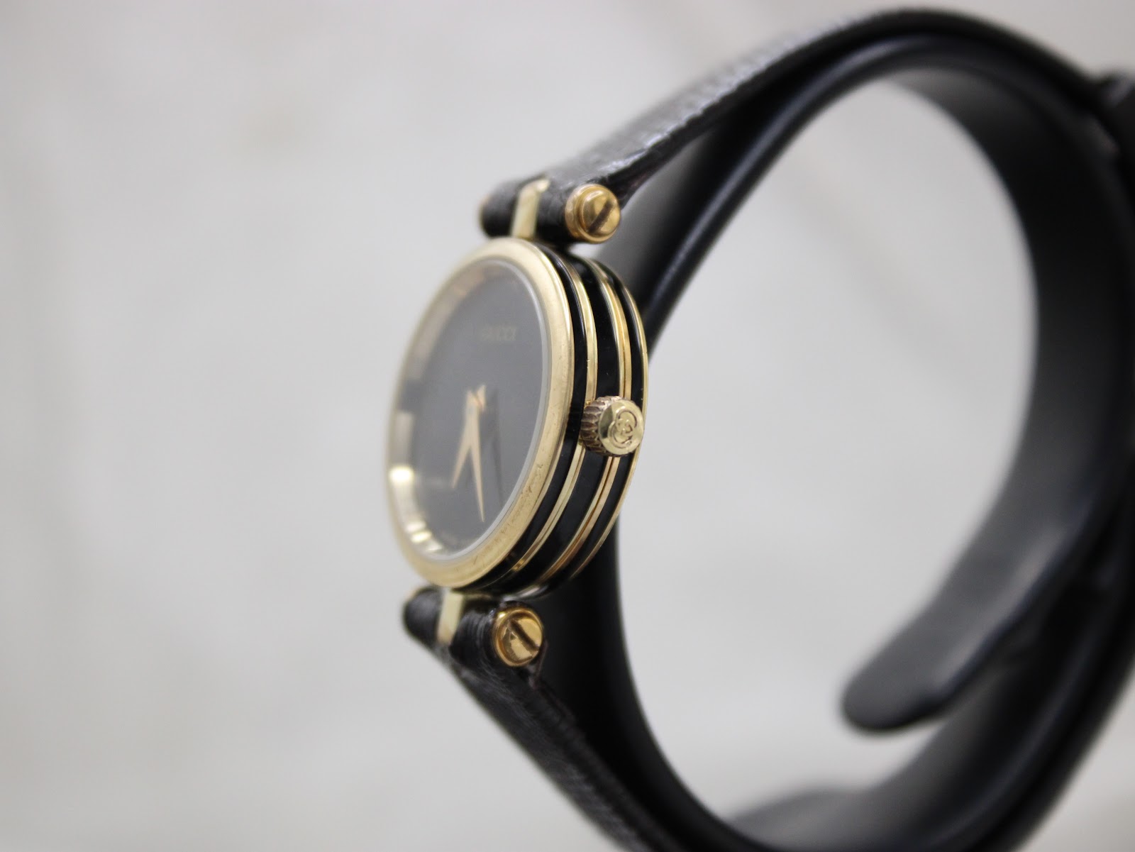 Side profile of the Gucci 2000L watch on a display stand, showcasing its slim fluted gold-plated case and crown.