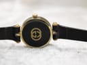 Close-up of the watch case back, showing the iconic Gucci interlocking G logo in gold against a black background.