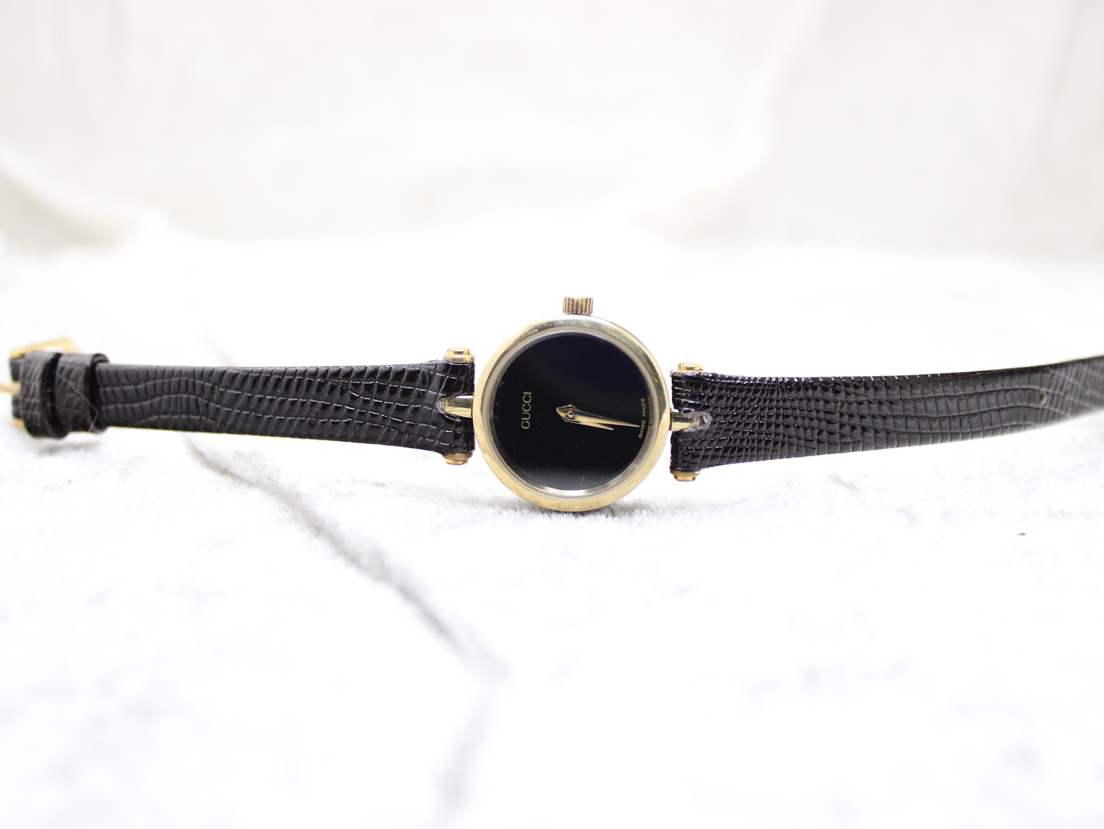 Overhead view of the entire Gucci 2000L watch, displaying the long black leather strap and the round gold-plated case.