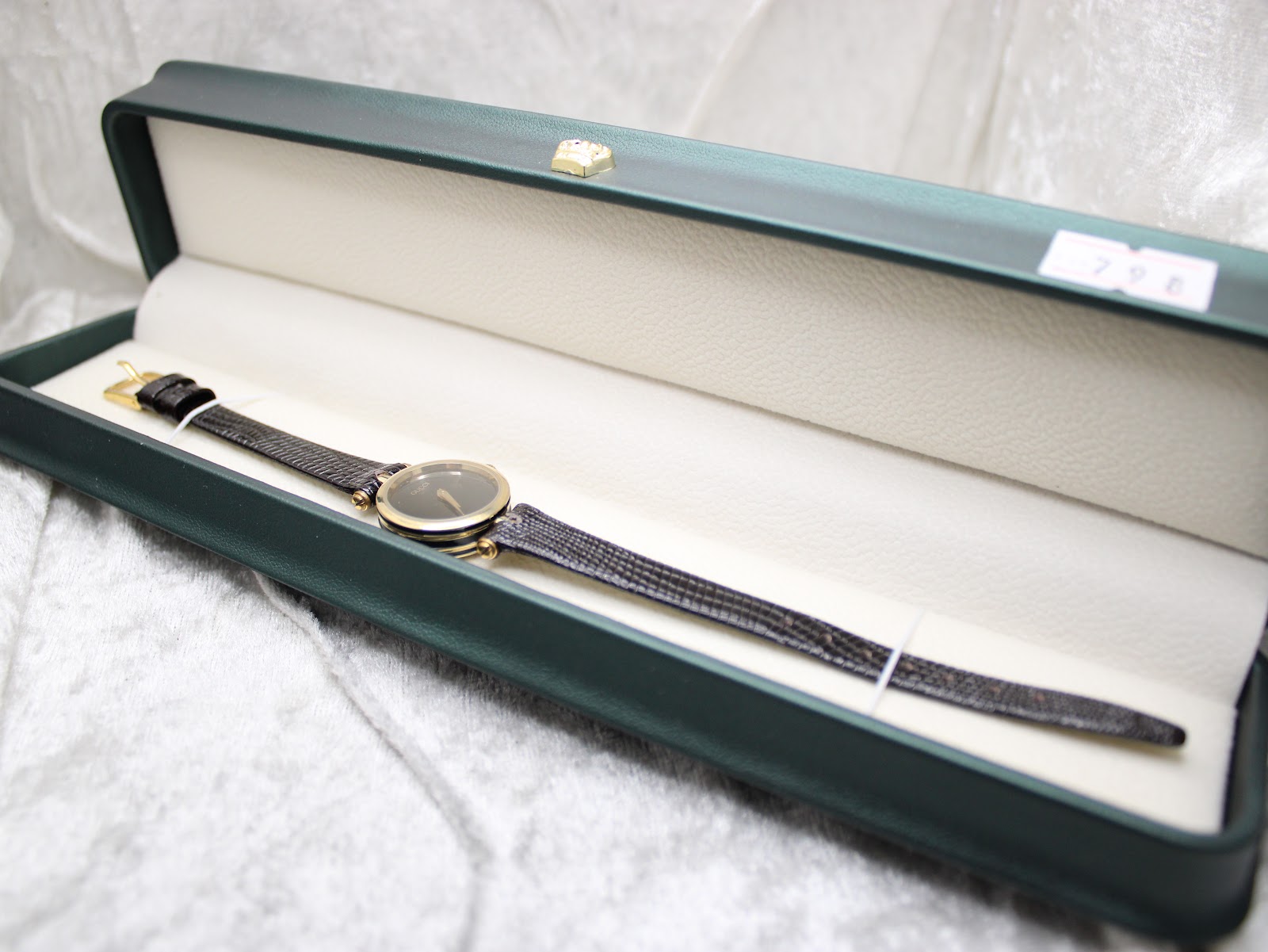 Overhead view of the Gucci 2000L watch resting inside a dark green presentation box with a cream-coloured interior.