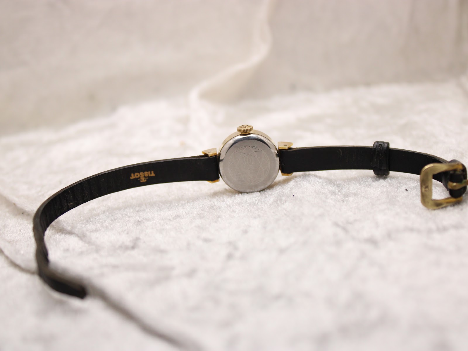 Full length back view of the Tissot watch on a display stand, illustrating the black leather strap and the buckle.