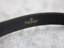 Detail shot of the interior of the black leather strap, clearly showing the embossed gold 'Tissot' logo.