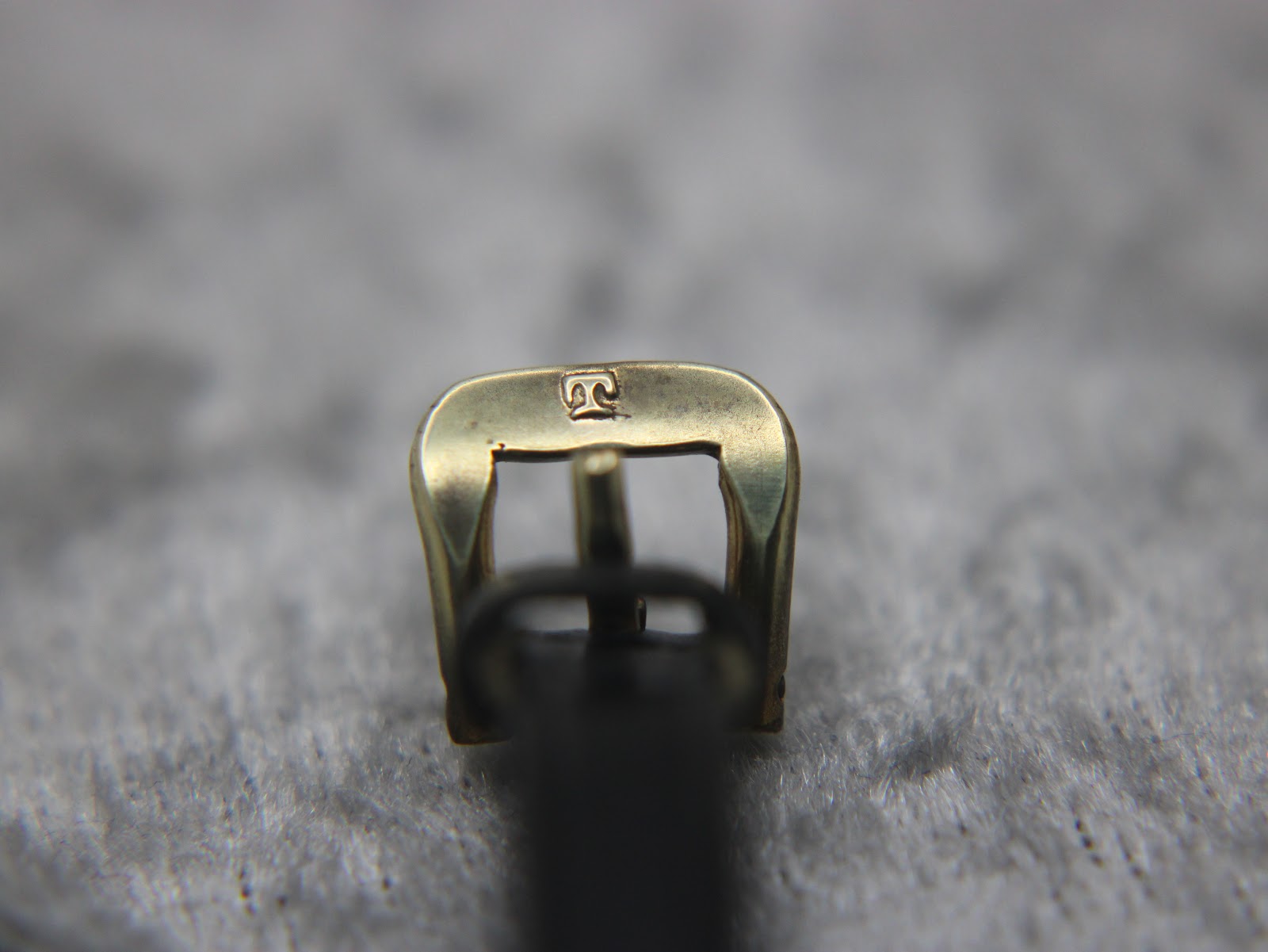 Close-up of the gold-toned buckle, featuring the distinctive Tissot 'T' logo.