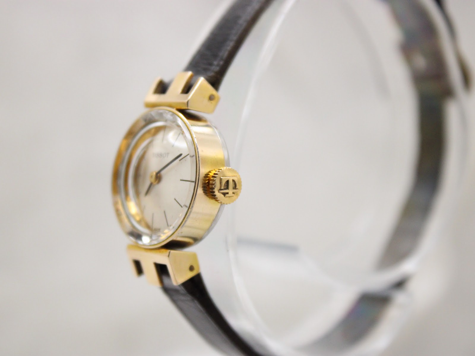 Oblique view of the Tissot watch from the right, highlighting the signed crown and the gold-plated case.