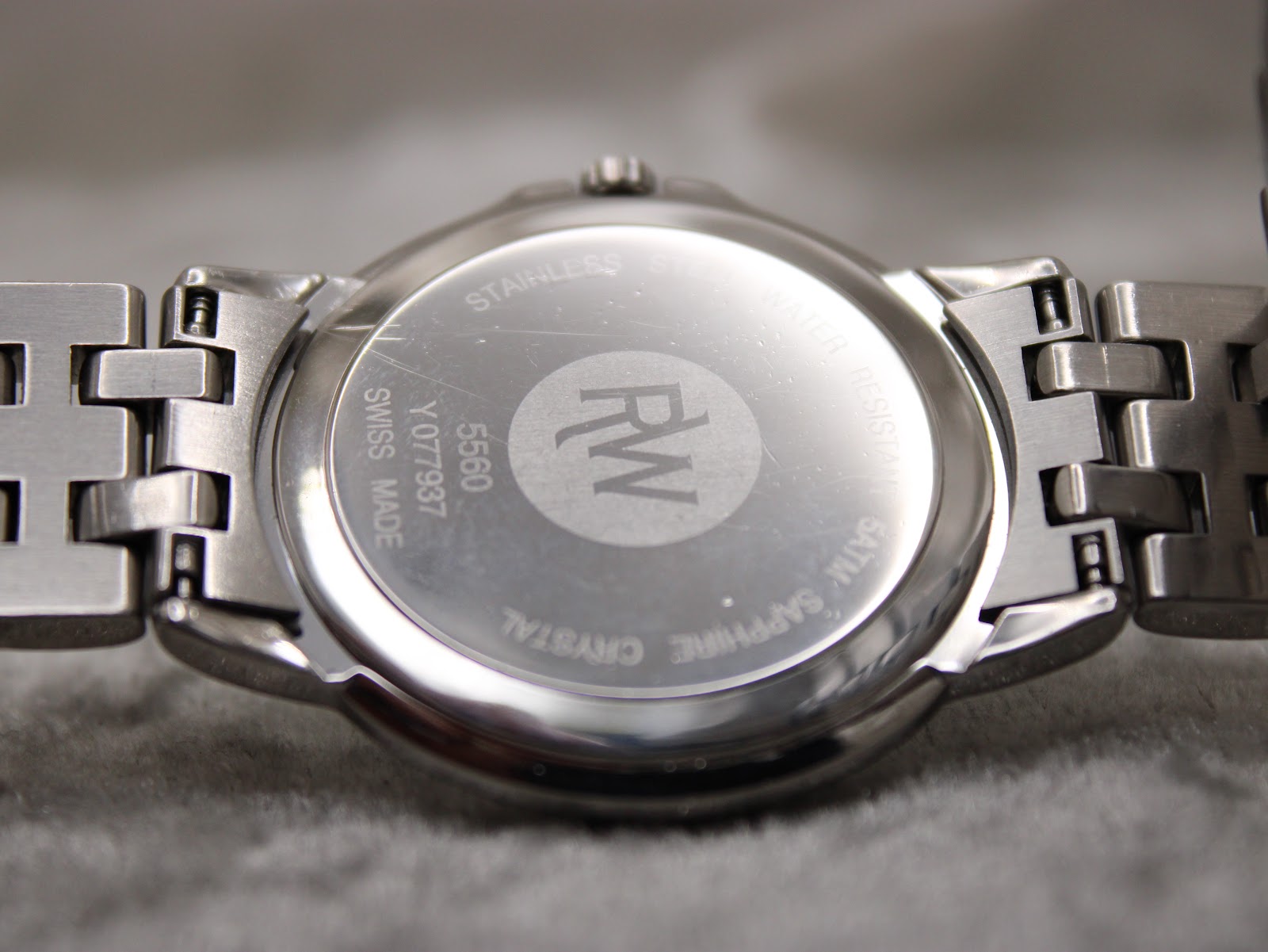 Close-up of the watch case back, showing "RAYMOND WEIL", "STAINLESS STEEL", "WATER RESISTANT 5ATM", "SAPPHIRE CRYSTAL", "SWISS MADE", and model reference 5560.
