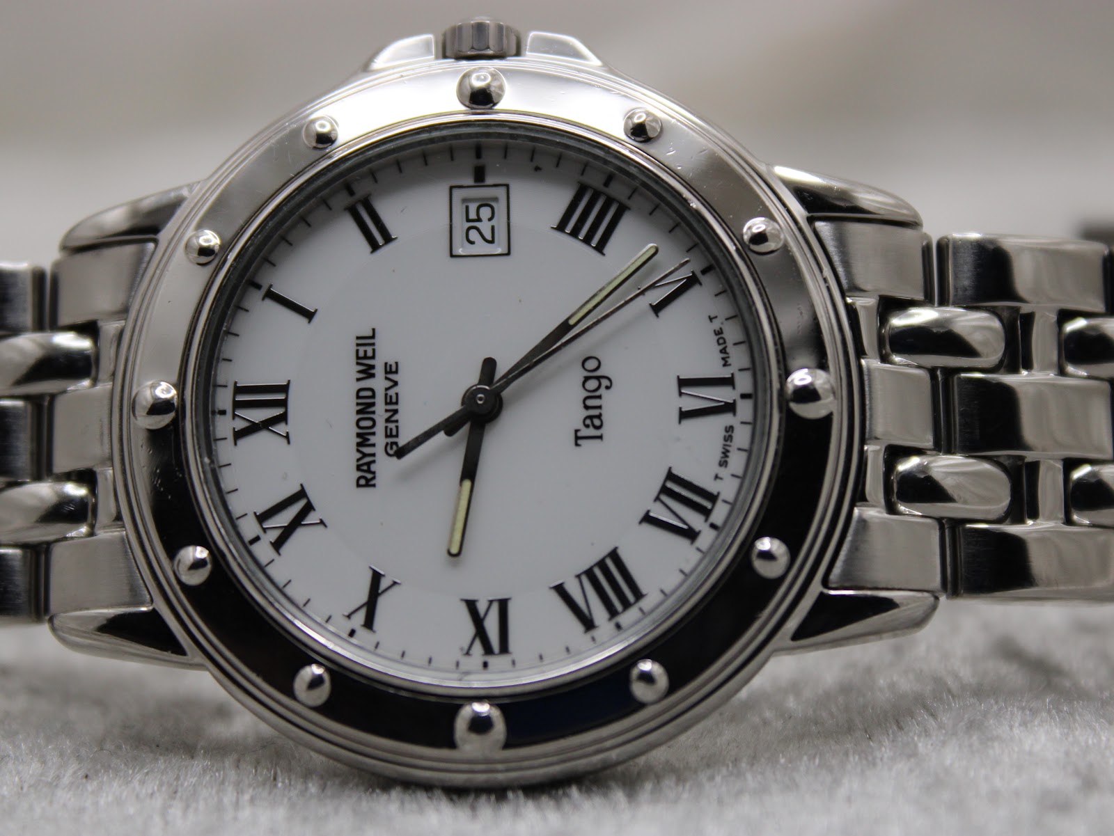 Macro close-up of the Raymond Weil Tango's white dial, detailing the black Roman numerals, minute track, RW logo, and date window.