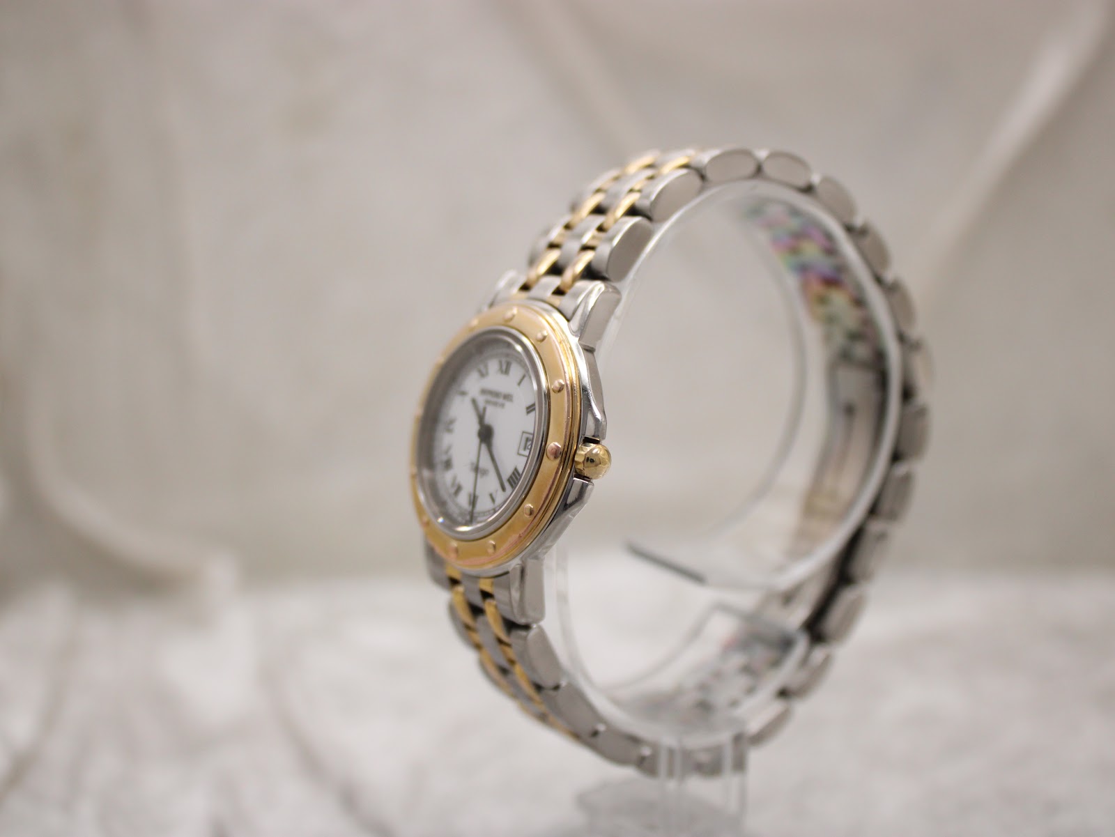 Side profile view of the Raymond Weil Tango watch, showcasing the two-tone bracelet and case on a clear stand.