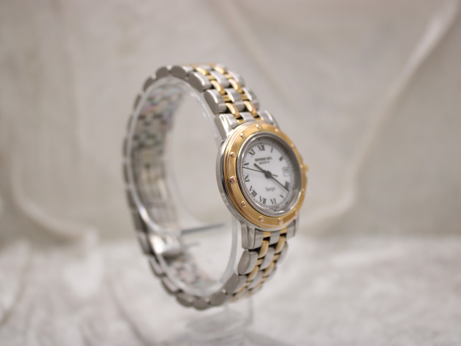 Angled three-quarter view of the Raymond Weil Tango watch, highlighting the contrasting gold-tone bezel with decorative screws and integrated two-tone bracelet.