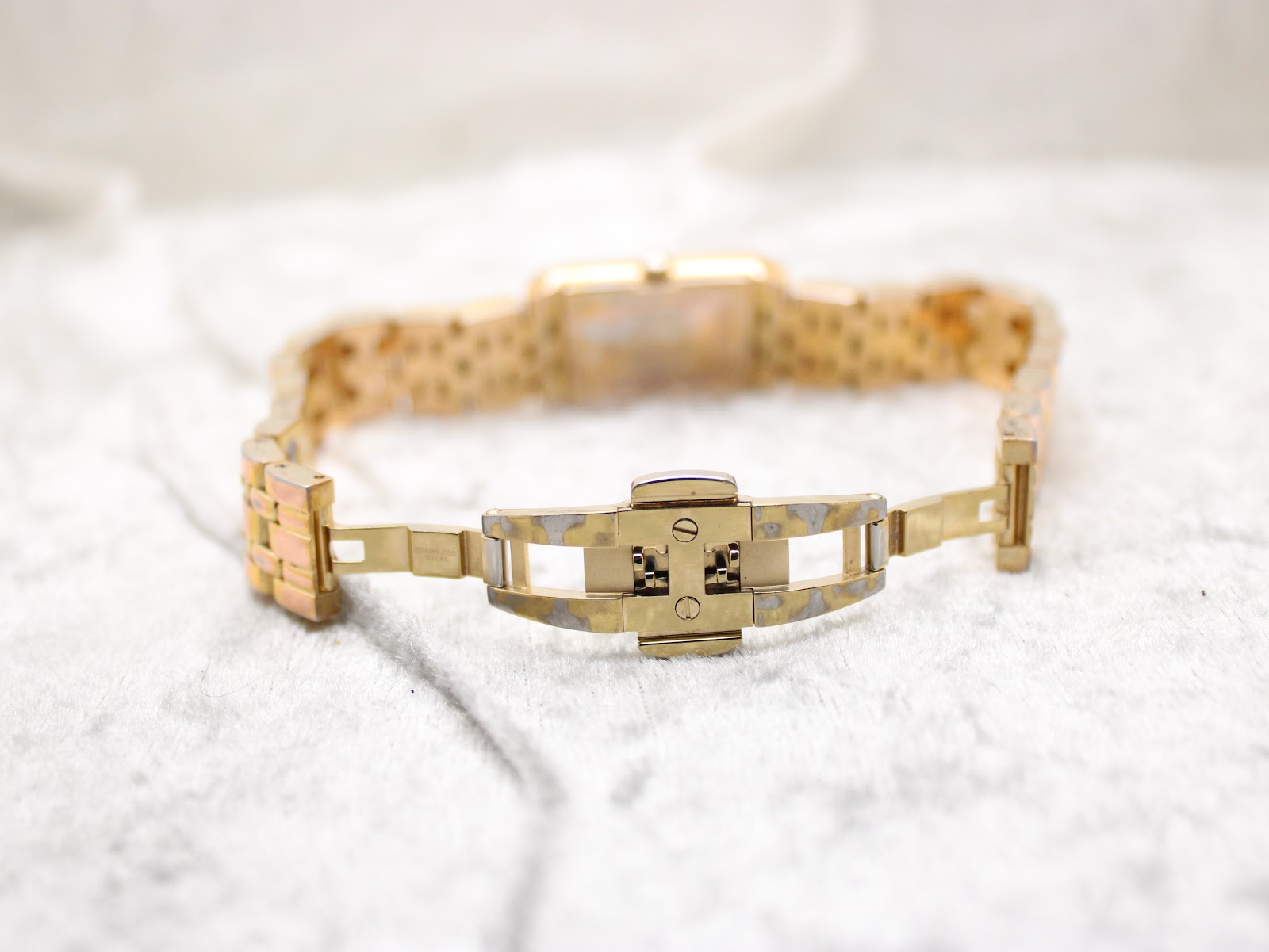 Detailed view of the open butterfly clasp on the gold-tone Raymond Weil bracelet, showing minor wear.