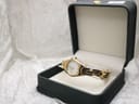 Tissot G349 watch resting in an open dark green presentation box with a cream interior on a white textured background.