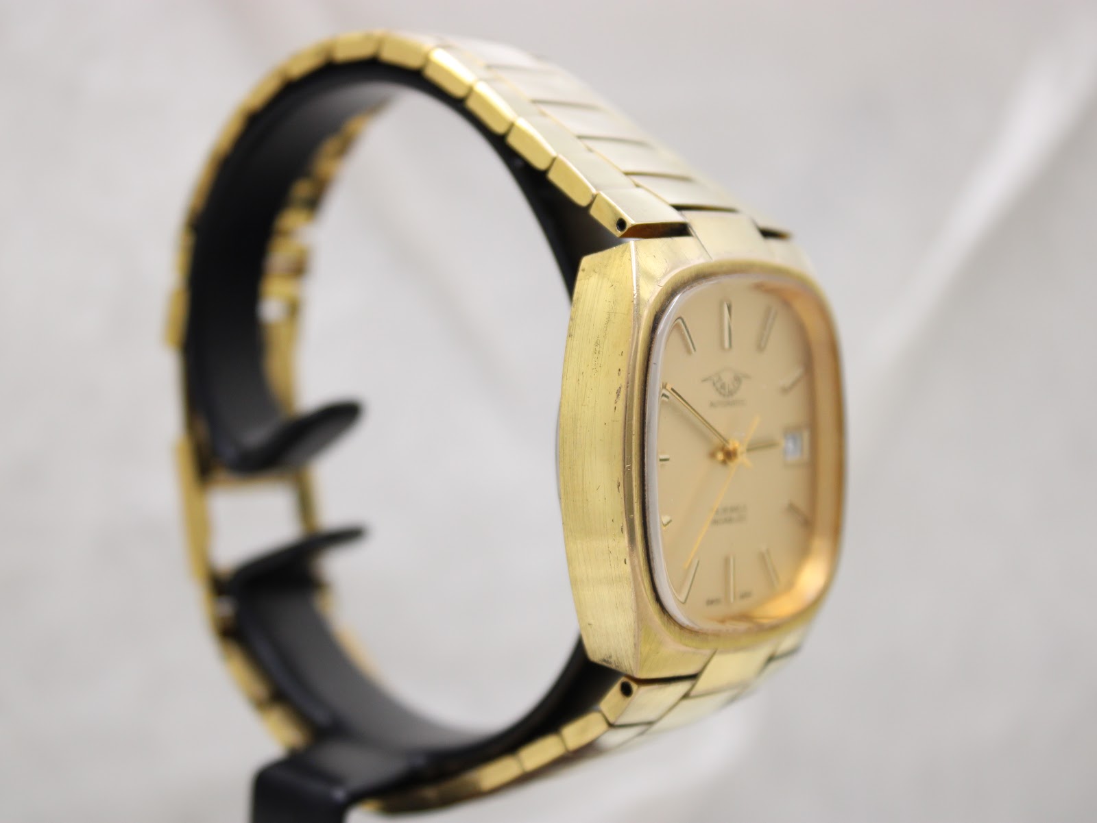 Left-side view of the gold-tone Talis watch, showing the cushion case profile and bracelet on a display stand.
