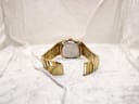 Back view of the entire gold-tone Talis watch and bracelet, showing the open folding clasp on a white textured surface.