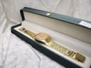 The gold-tone Talis watch resting inside an open green display box with a cream interior.