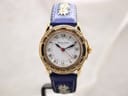 Front view of Michel Jordi Genève gold-tone watch with white Roman dial and blue embroidered strap on a stand.