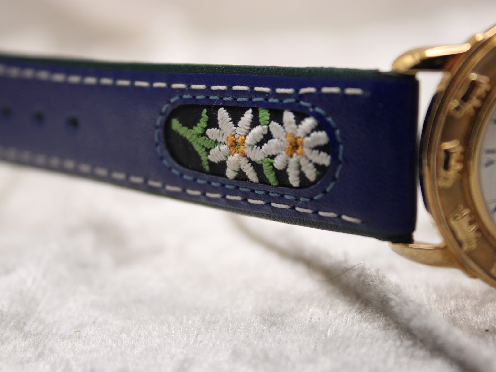 Close-up of the embroidered floral motif, likely an edelweiss, on the blue leather strap.