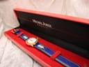 Overhead view of the Michel Jordi Genève watch inside its red presentation box with black interior.