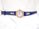 Full view of the Michel Jordi Genève watch and its blue embroidered leather strap laid flat on a white surface.