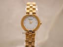 Front view of Raymond Weil Genève ladies gold-tone watch with white mother of pearl dial and crystal markers, on a clear stand.