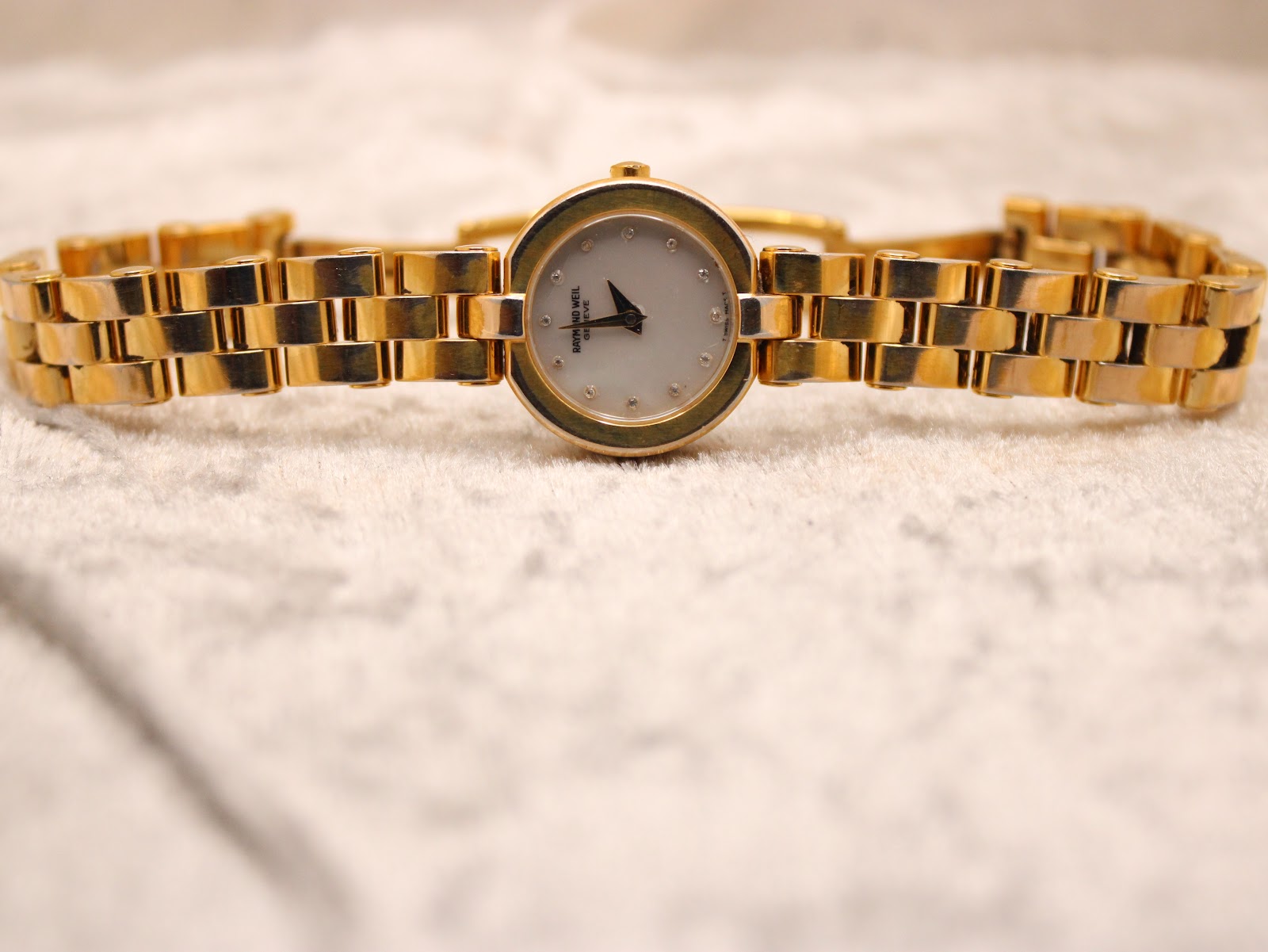 Top-down view of the watch lying flat on a textured white surface, with the bracelet extended.