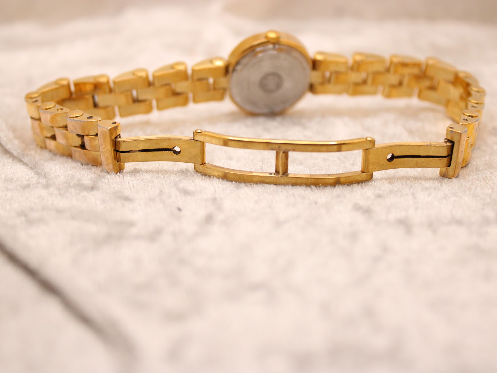View of the watch back and extended bracelet with the folding clasp open, on a textured white surface.